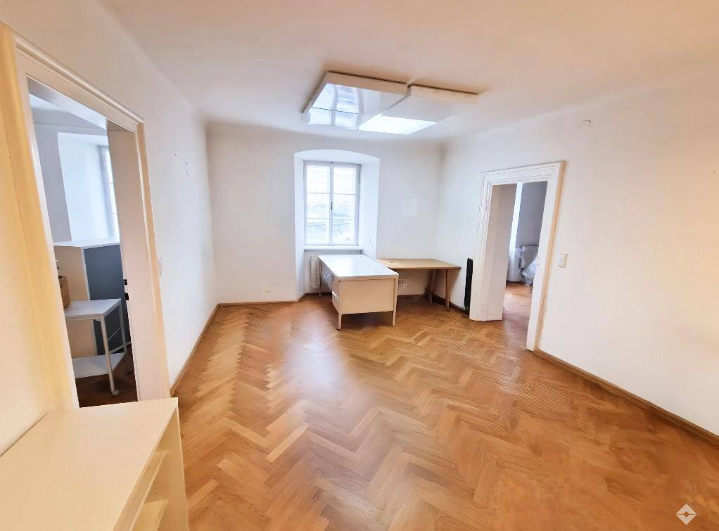 Großes Büro mit Einbauschränken, Fischgrätparkett und einer dekorativen Stuckdecke, gut beleuchtet.