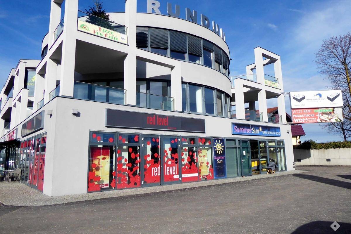 Geräumiger Büroraum mit grauem Teppichboden, großen Fenstertüren und Zugang zu einem Balkon.