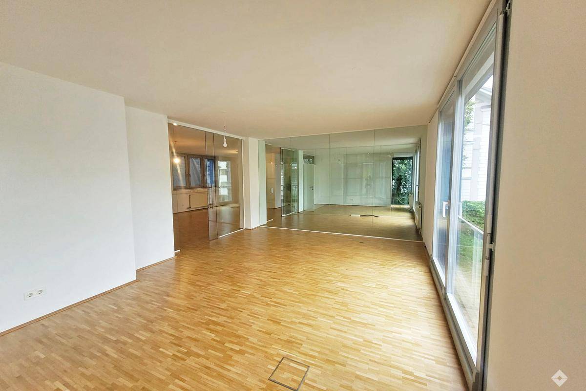 Geräumiger, heller Raum mit Parkettboden, großen Fenstern und verspiegelten Wänden, ideal für Wohnen oder Büro.