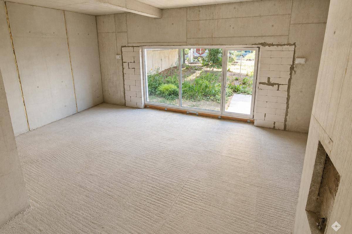 Unfertiger Raum mit großen Schiebefenstern, die einen Blick auf den Garten und viel Tageslicht bieten.