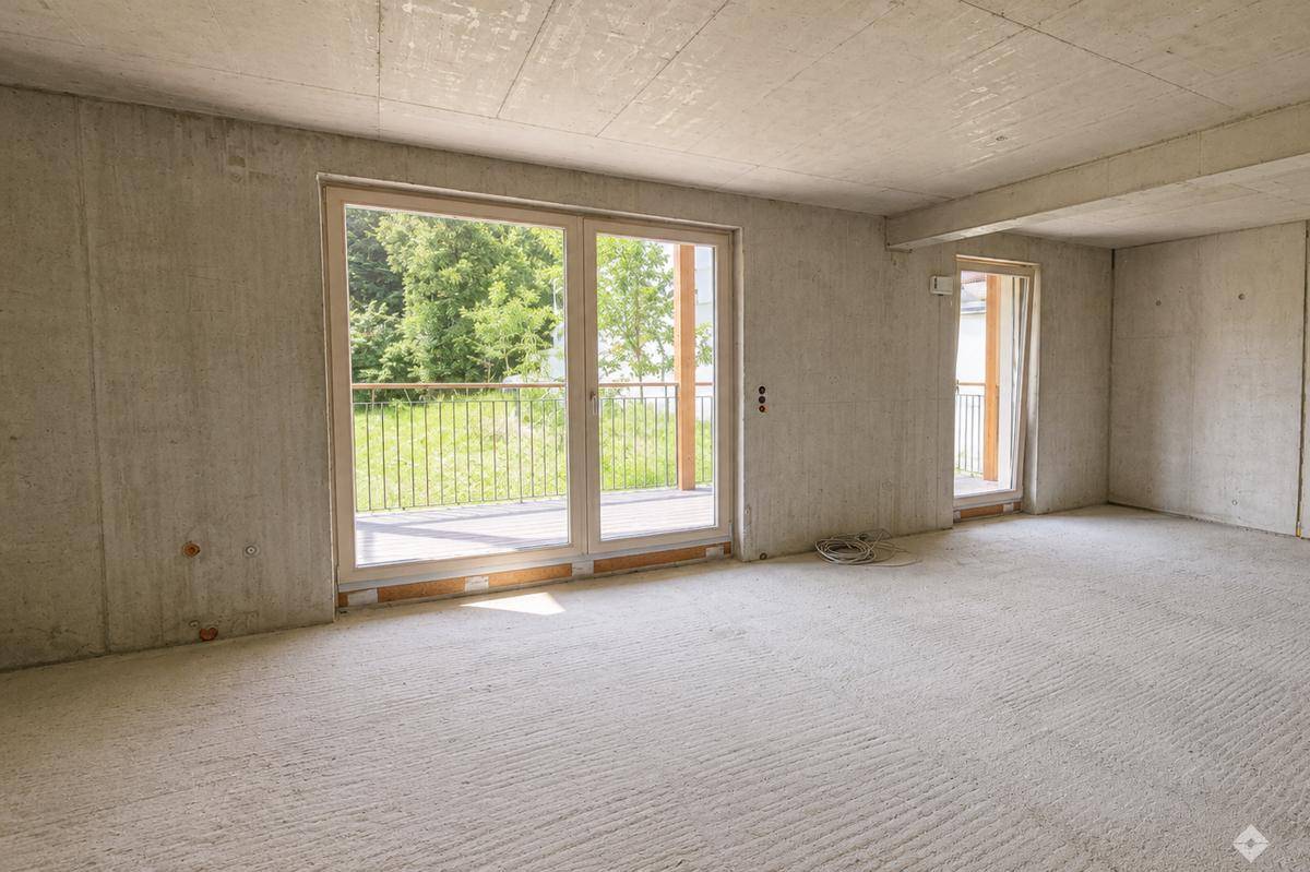 Unfertiger Innenraum mit großen Fenstern und Zugang zu einem Balkon, der viel natürliches Licht hereinlässt.