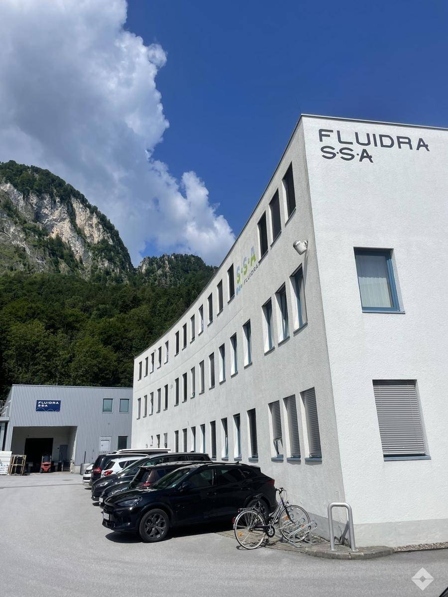 Modernes Geschäftsgebäude mit geschwungener weißer Fassade, Parkplätzen und Bergblick.