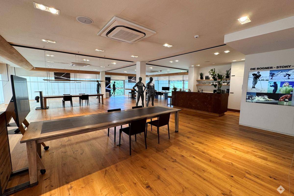 Geräumiger Verkaufsraum mit Holzboden, modernen Möbeln und einer Multimedia-Wand für Präsentationen.