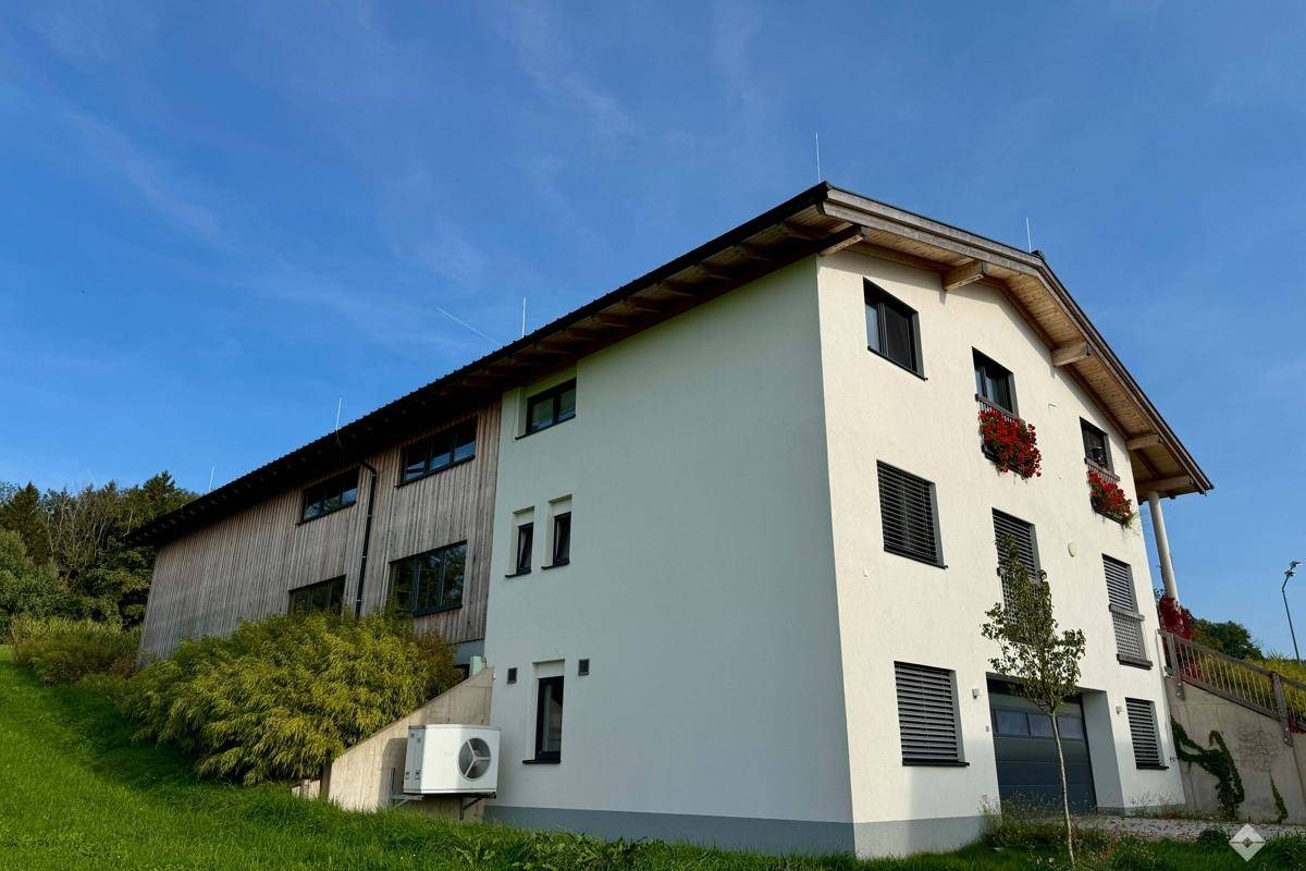 Rückansicht des Gebäudes mit weißer Fassade, Holzverkleidung und Außenklimaanlage.