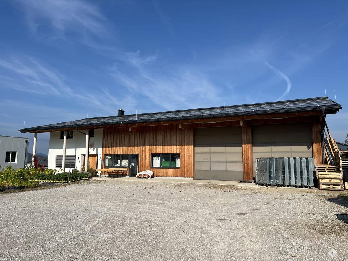 Modernes Gebäude mit Holzfassade, großen Garagentoren und Photovoltaikanlage auf dem Dach.
