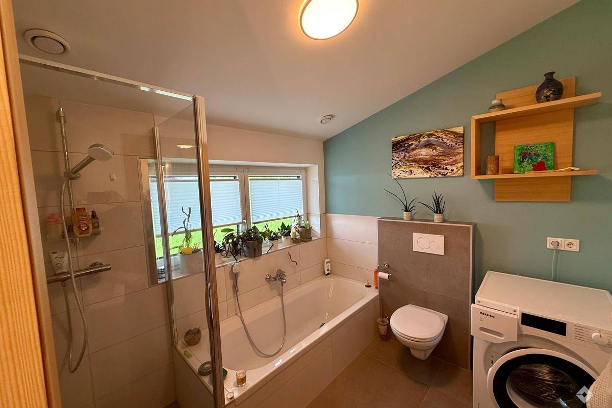 Modernes Badezimmer mit Dusche, Badewanne, WC und Waschmaschine, in hellen Farben gehalten.