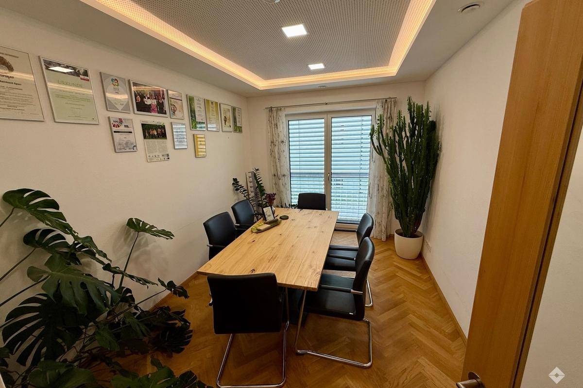 Konferenzraum mit Holztisch, schwarzen Stühlen und indirekter Deckenbeleuchtung.