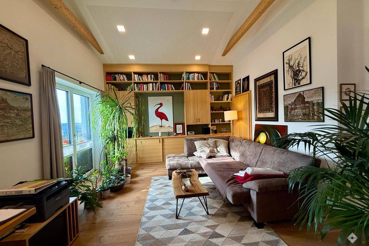 Geräumiges Wohnzimmer mit großem Sofa, Bücherregal und vielen Pflanzen, hell und einladend.