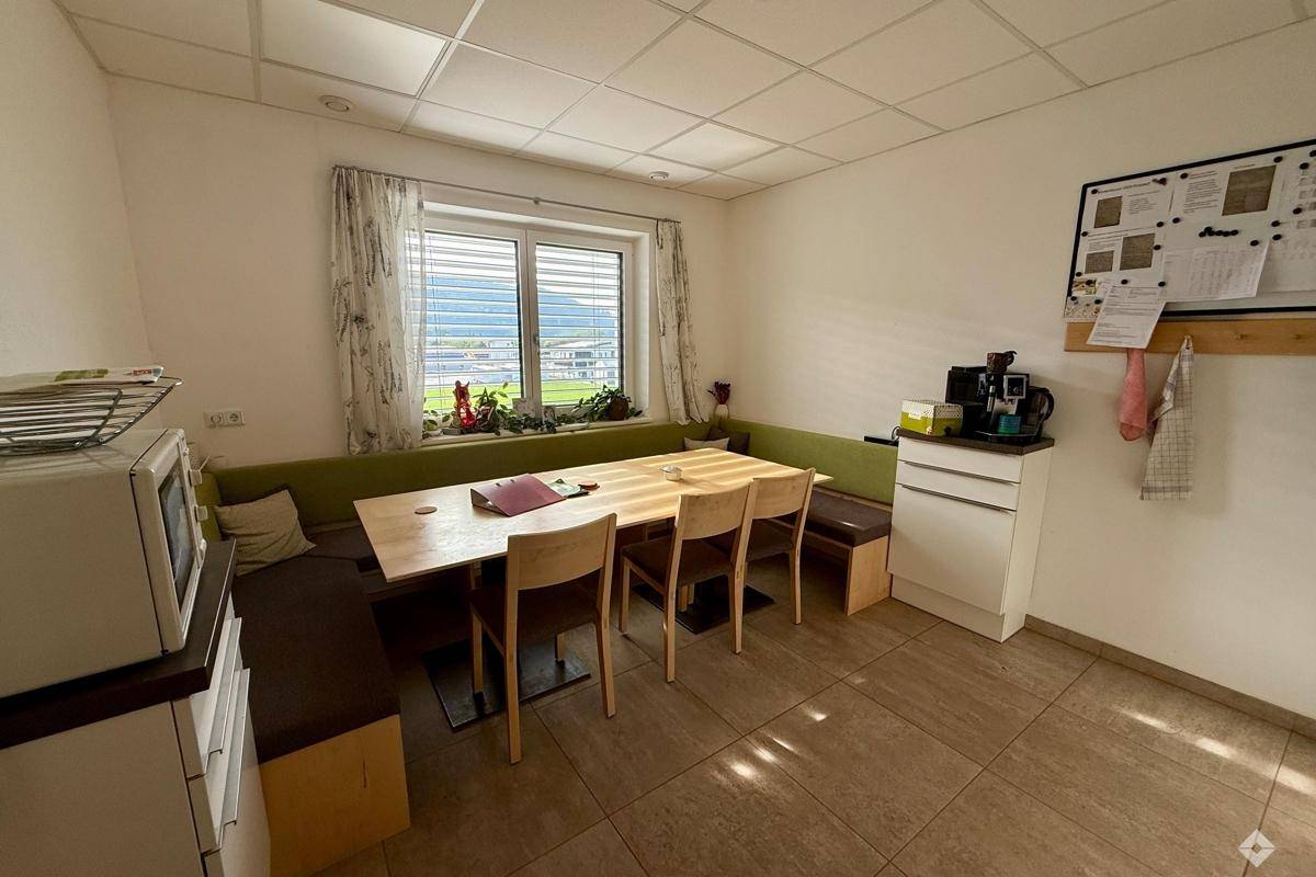 Gemütlicher Pausenraum mit Essecke, Fenster und kleiner Küchenzeile.