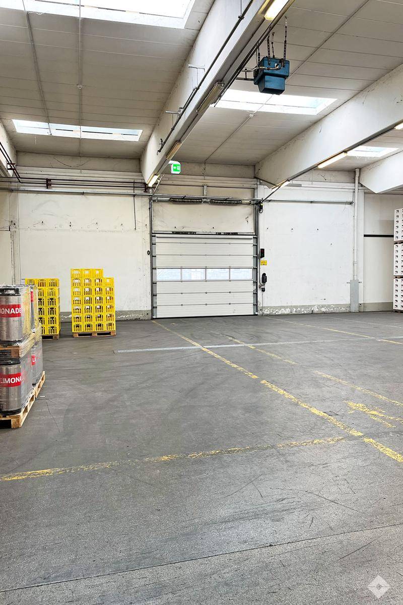 Helle Lagerhalle mit einem weiteren Rolltor, Oberlichtern und gelben Kisten, bereit für den Warentransport.