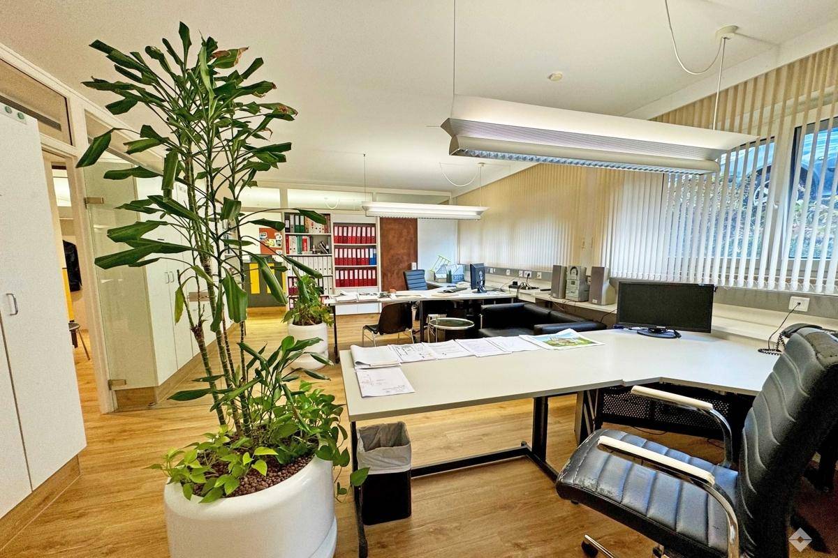 Funktionales Büro mit mehreren Arbeitsbereichen, Pinnwand und Fenstern mit vertikalen Jalousien.