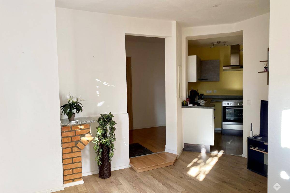 Heller Wohnbereich mit Holzboden, dekorativem Kamin und offenem Zugang zur Küche.