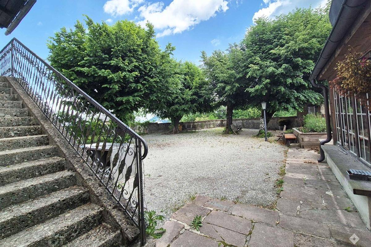 Großer Kiesgartenbereich mit alten Bäumen, Steinmauern und einer Außentreppe.