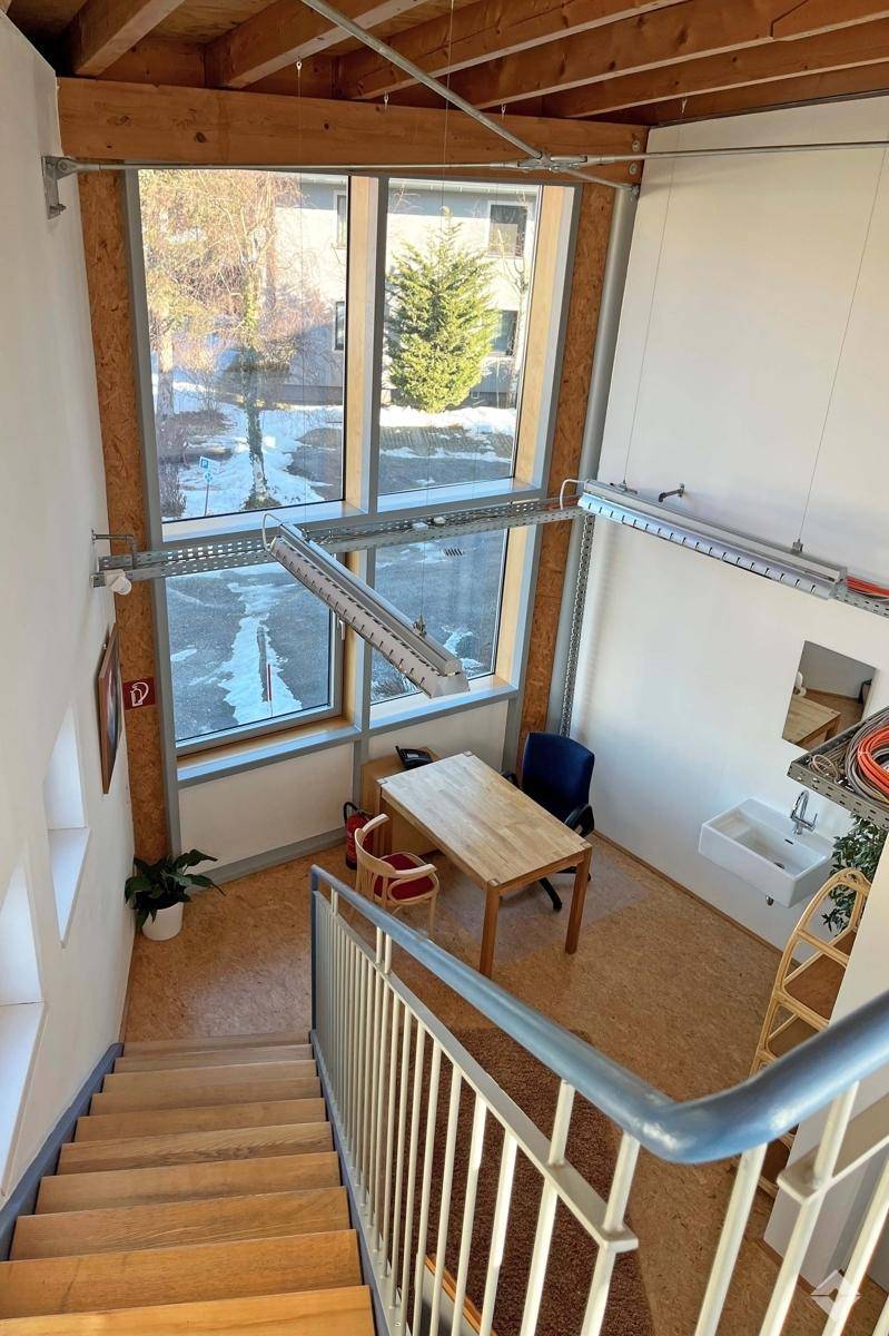 Helles Büro mit großen Fenstern, Holztisch und Blick auf die verschneite Umgebung mit Bäumen.