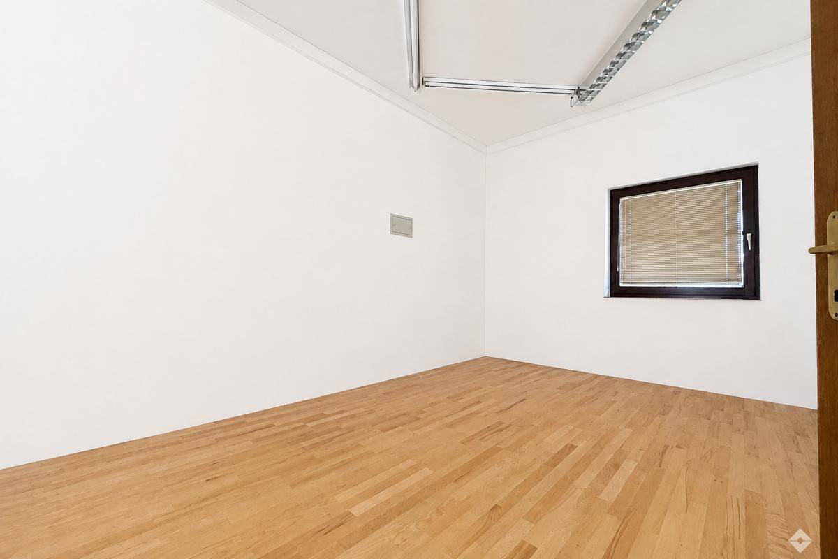 Großer, leerer Büroraum mit hellem Holzfußboden, weißen Wänden und Rasterdeckenbeleuchtung.