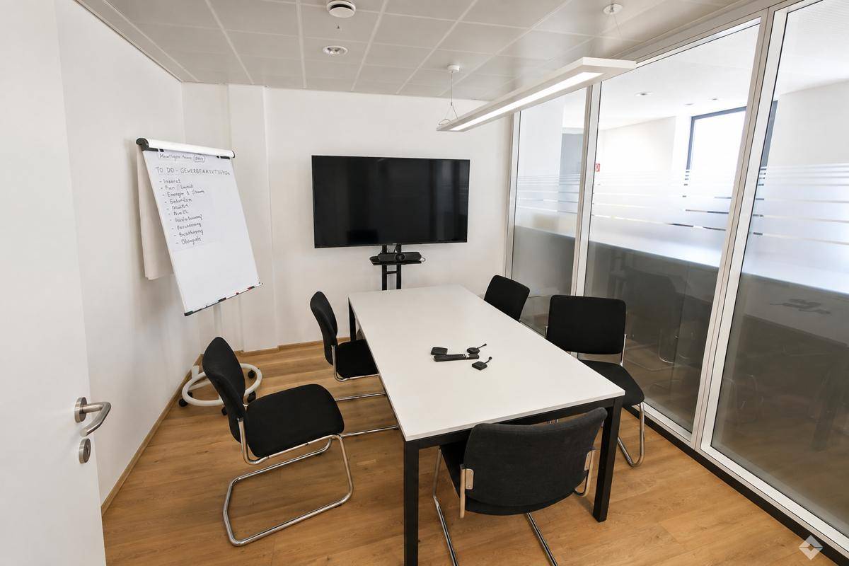 Konferenzraum mit großem Bildschirm, Whiteboard und Glastrennwand für Besprechungen.