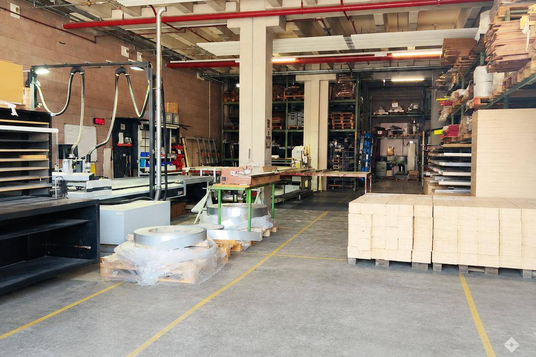 Geräumige Lagerhalle mit hohen Decken, Industriemaschinen und gestapelten Materialien auf Paletten.