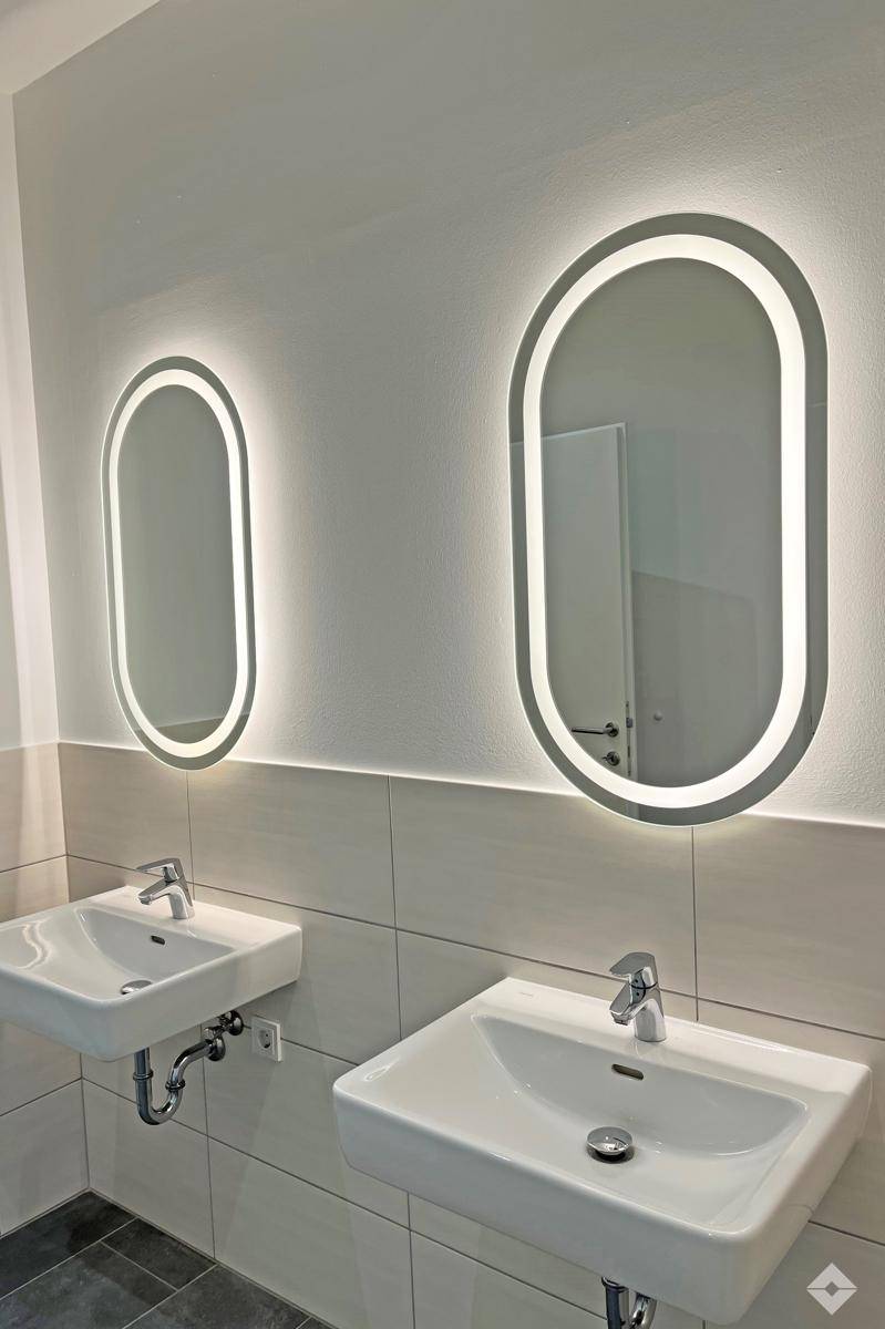 Modernes Badezimmer mit zwei Waschbecken und stilvollen, beleuchteten Spiegeln.