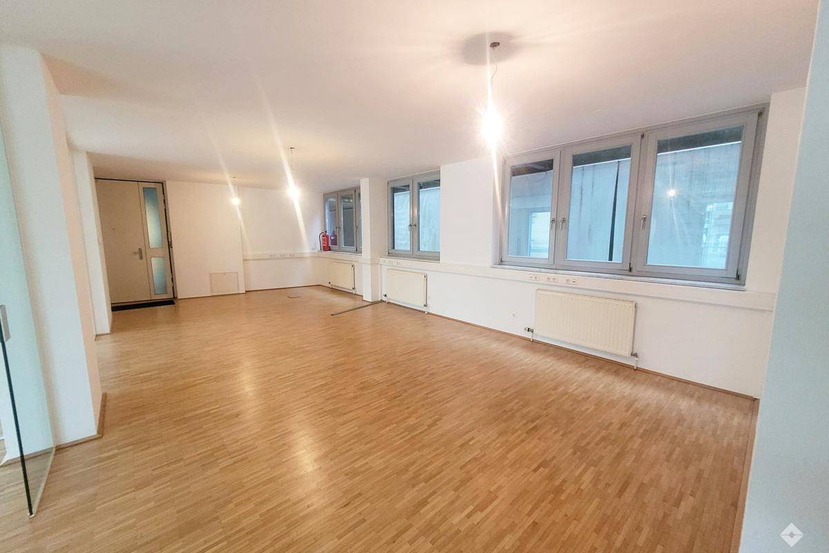 Großer, heller Raum mit Parkettboden, mehreren Fenstern und Heizkörpern unter den Fensterbänken.