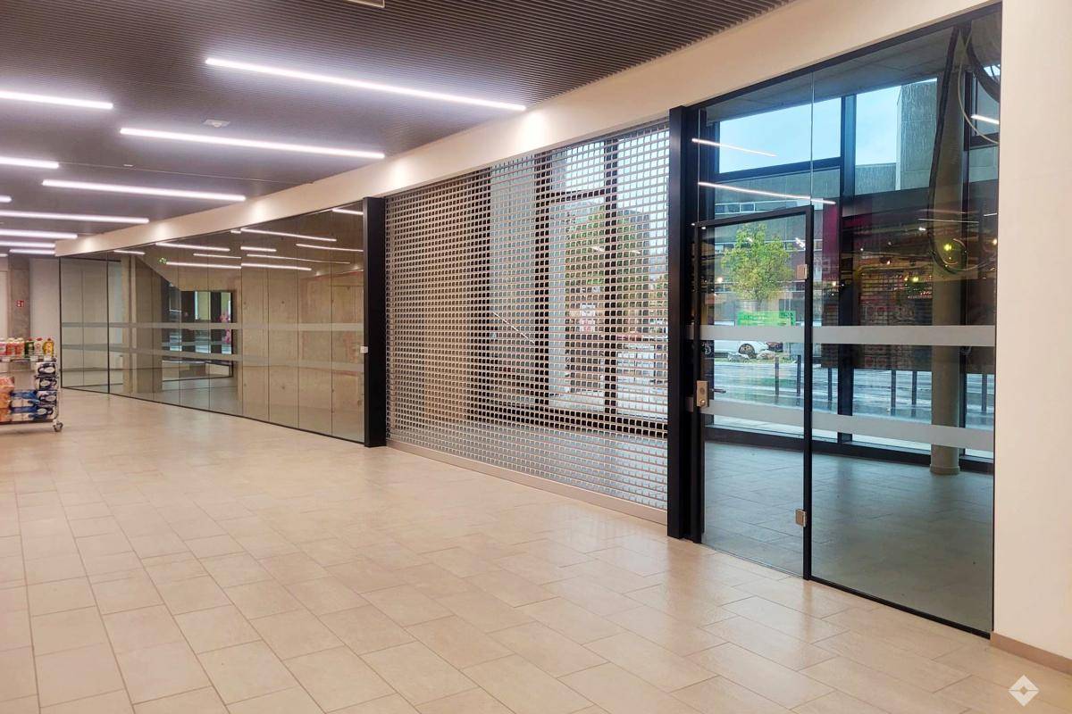 Moderner Gewerberaum mit großen Glasfronten und Metallrollgitter, ideal für Ladenlokale in einem Einkaufsbereich.