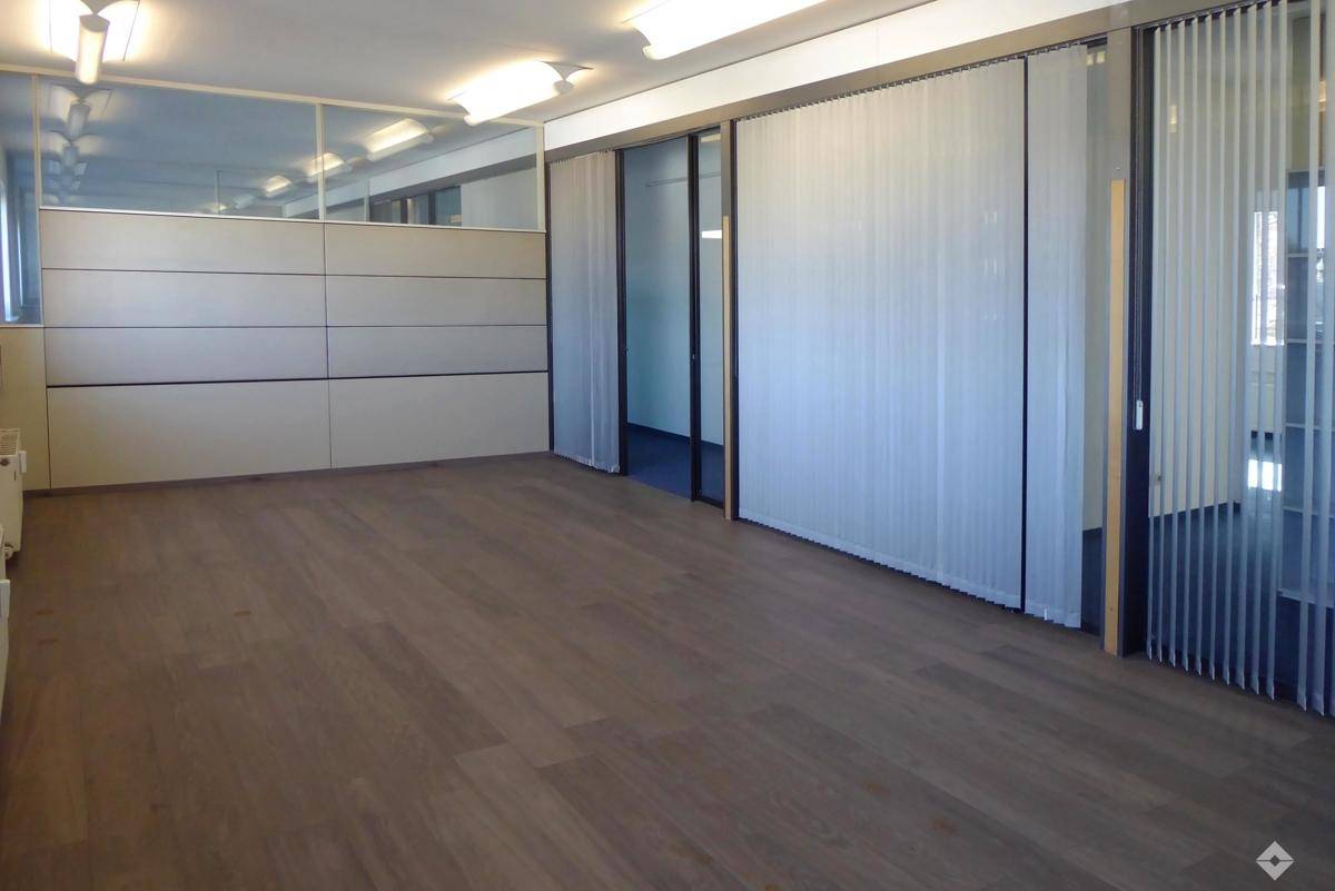 Heller Büroraum mit Holzfußboden und vertikalen Jalousien an den Glastrennwänden.