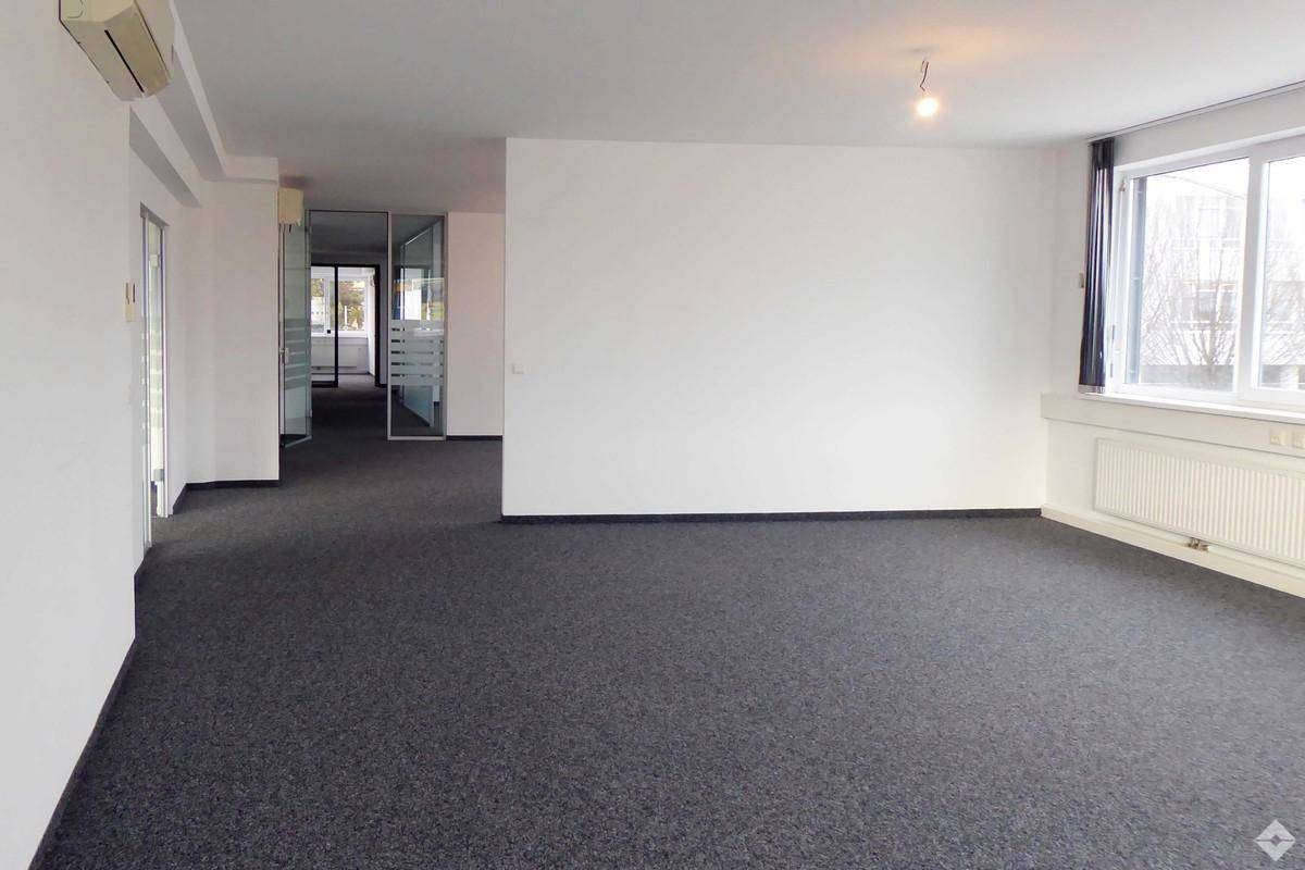 Großzügiger Bürobereich mit Teppichboden und Blick auf weitere Büroräume durch Glastüren.