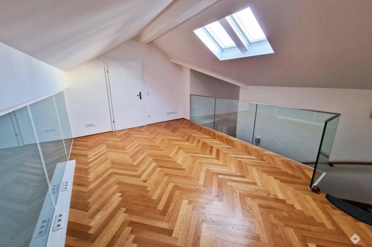 Offener Galeriebereich mit Glasgeländer, Fischgrätparkett und Dachfenster für zusätzliche Helligkeit.