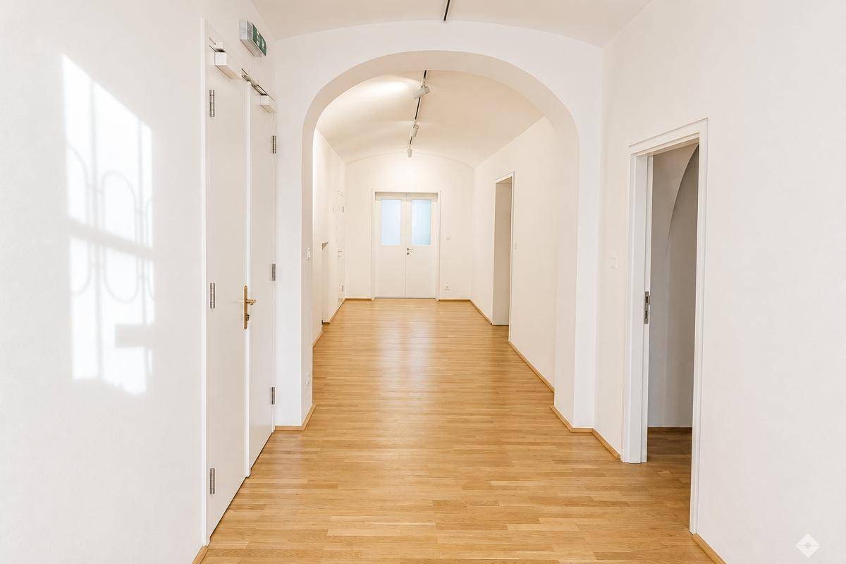 Langer, heller Flur mit Holzboden, weißen Wänden und mehreren Türen, der zu weiteren Räumen führt.