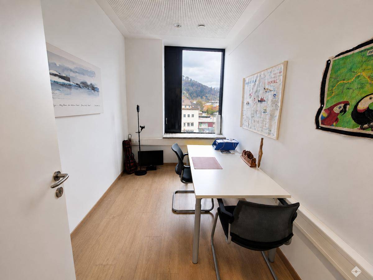 Kleines, helles Büro mit Schreibtisch, Stuhl und Fensterblick auf die hügelige Landschaft.