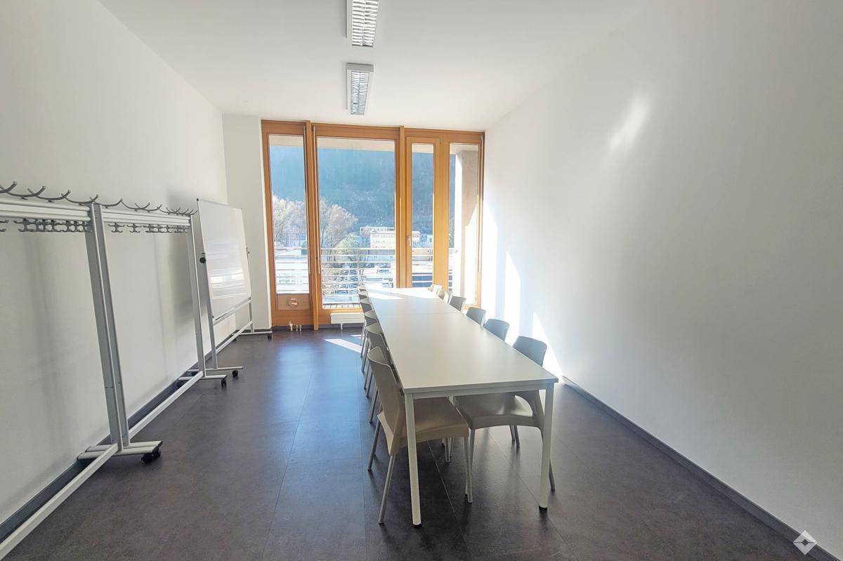 Langer Büroraum mit Tischen, Stühlen, Garderobe und großen Fenstern für viel Tageslicht.