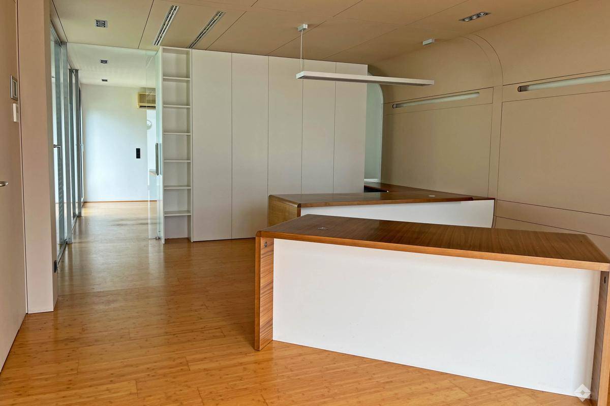 Heller Büroraum mit Holzboden, modernen Schreibtischen und integrierten weißen Schränken.
