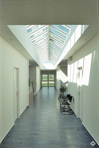Langer Flur mit hellem Oberlicht, das viel natürliches Licht hereinlässt und moderne Fliesenböden.