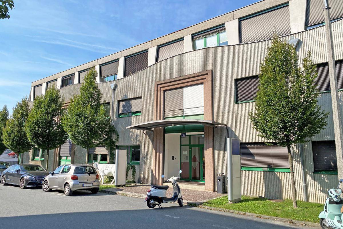 Modernes Bürogebäude mit strukturierter Fassade, vielen Fenstern und gepflegter Außenanlage mit Parkplätzen.