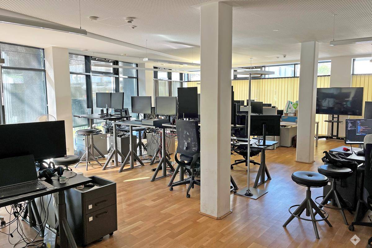 Großes, offenes Büro mit zahlreichen Arbeitsplätzen, Holzfußboden und viel Tageslicht durch die Fenster.