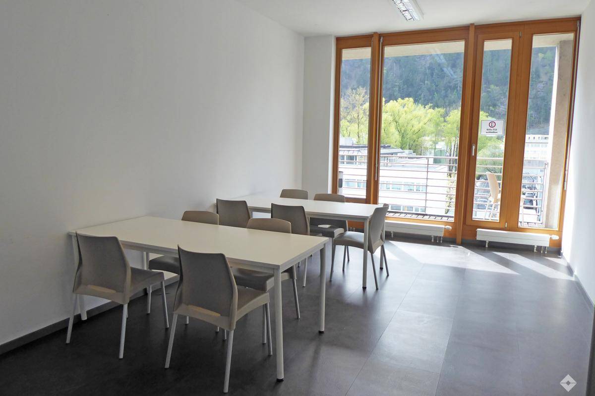Flexibler Büroraum mit mehreren Tischen, Stühlen und großen Fenstern mit Blick ins Grüne.
