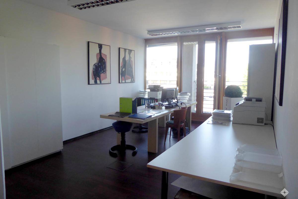 Funktionales Büro mit mehreren Arbeitsplätzen, dunklem Holzboden und großen Fenstern.