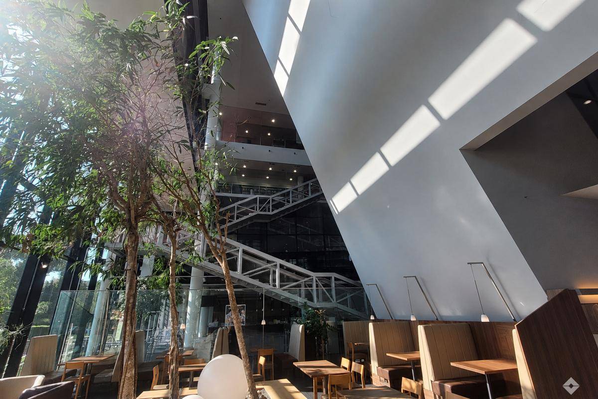 Großzügiger Cafébereich mit hohen Decken, viel Tageslicht und moderner Treppenarchitektur.