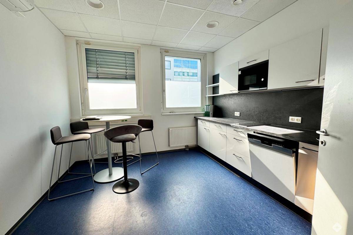 Funktionale Küchenzeile mit weißen Schränken, dunkler Arbeitsplatte und Stehtisch mit Hockern.