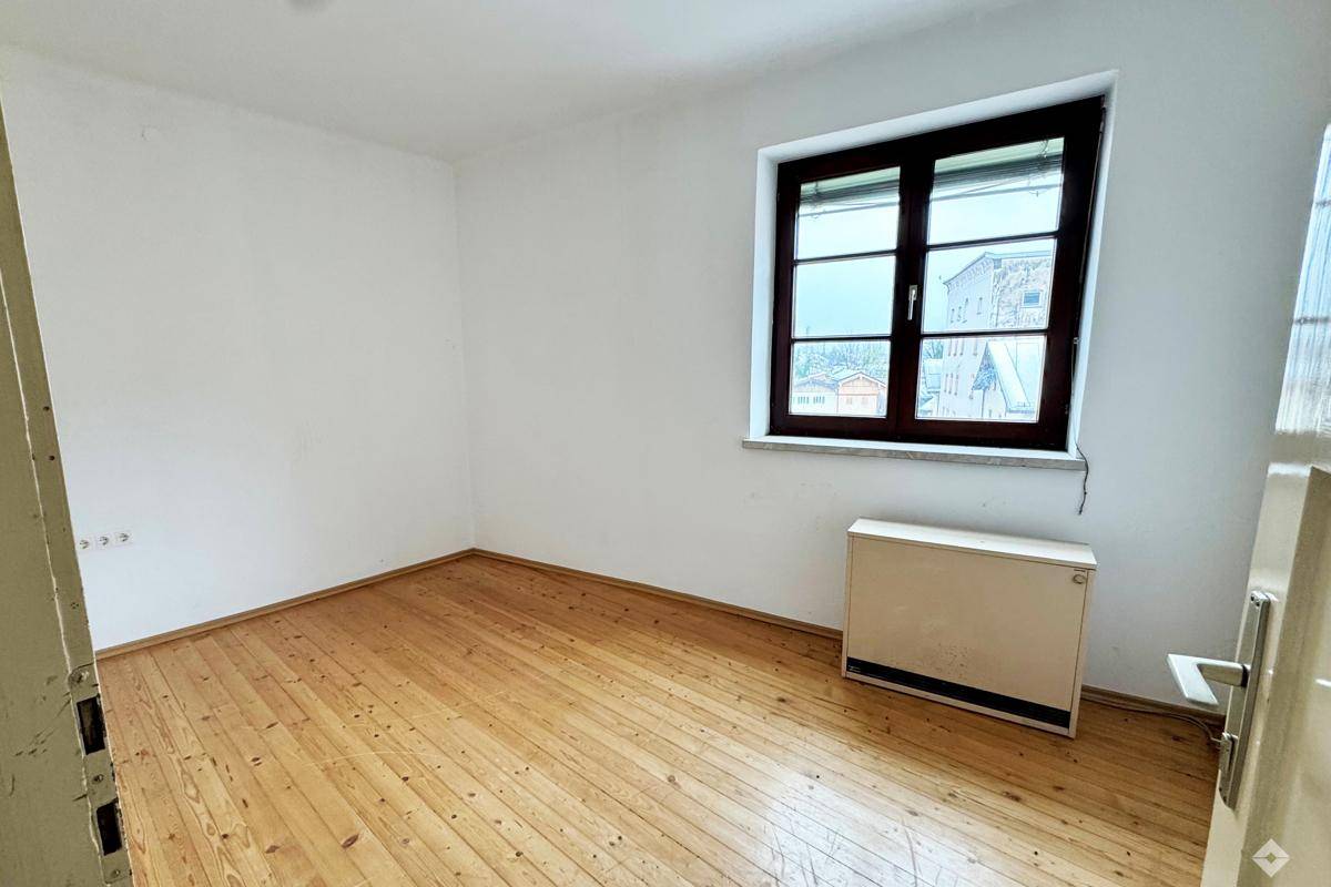 Helles Schlafzimmer mit Holzdielenboden und einem Fenster, das viel Tageslicht hereinlässt.