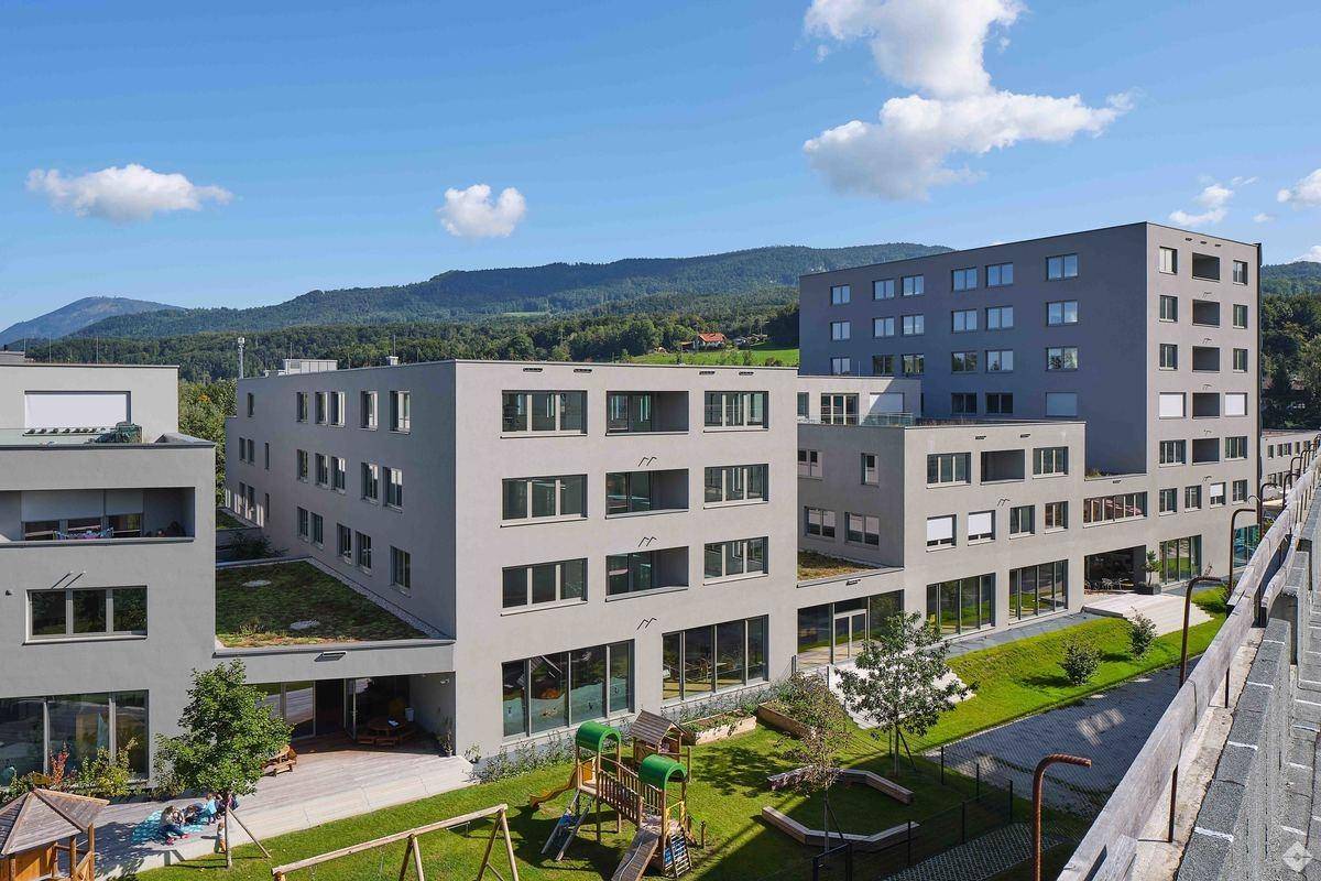 Moderne Wohnanlage mit mehreren Gebäuden, begrünten Dächern und einem Kinderspielplatz im Vordergrund.