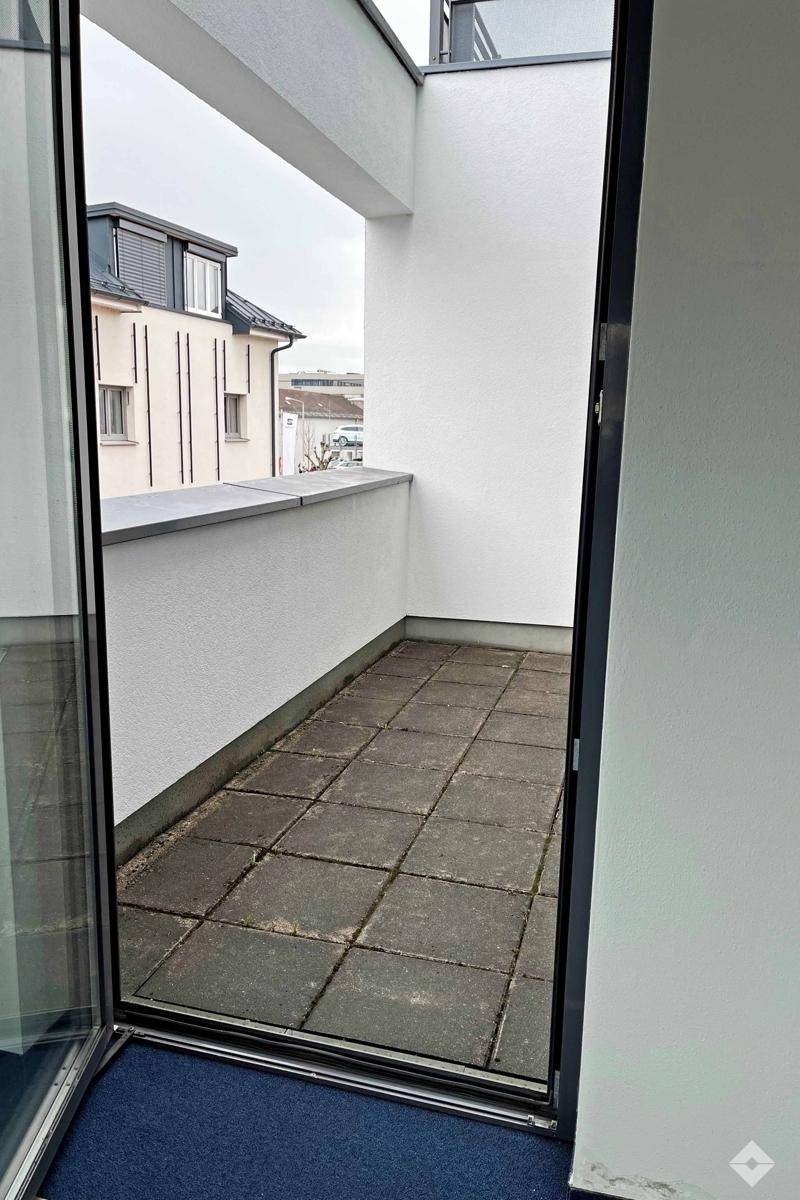 Überdachte Loggia mit Fliesenboden und Blick auf die umliegenden Gebäude und Dächer.