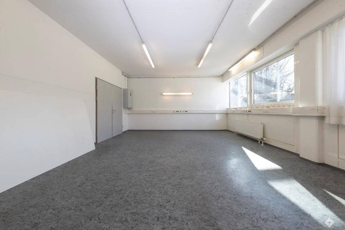 Modern eingerichtetes Büro mit mehreren Arbeitsplätzen, großen Fenstern und Blick in einen angrenzenden Bereich.