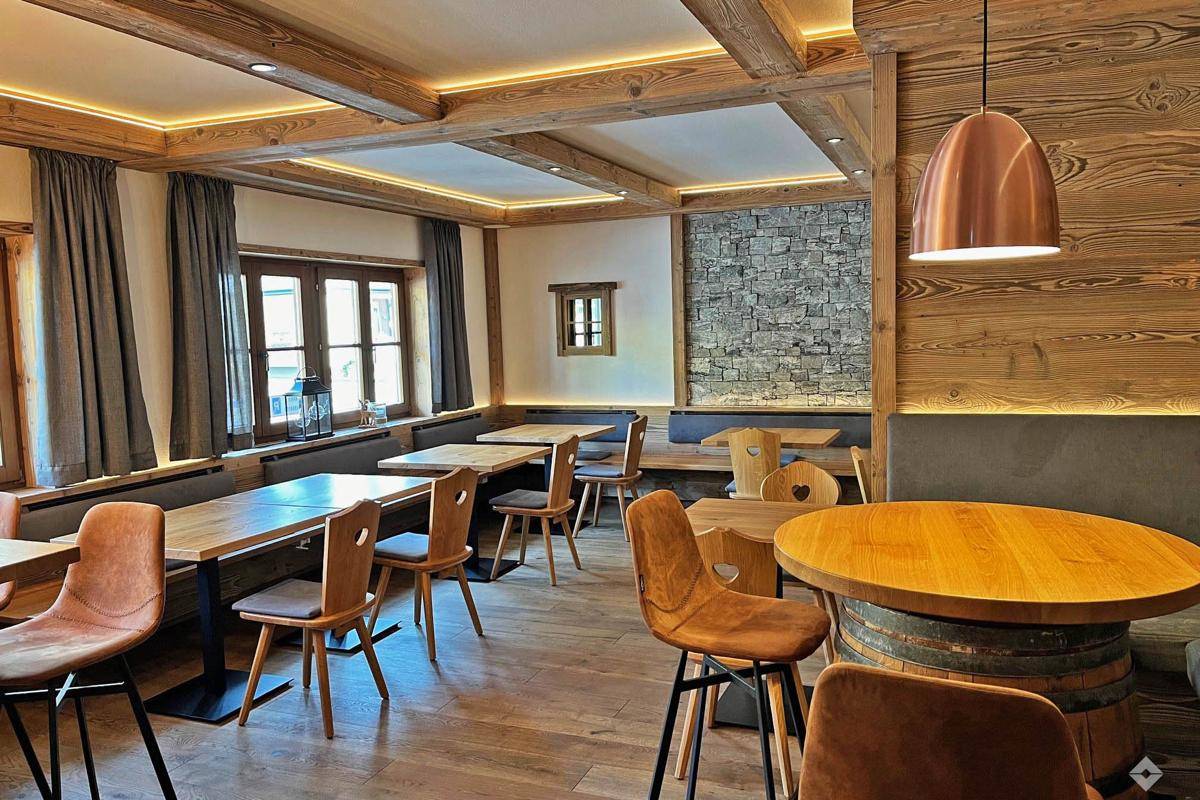 Gemütlicher Speisesaal mit Holztischen, Bänken und sichtbaren Deckenbalken sowie Steinakzenten.