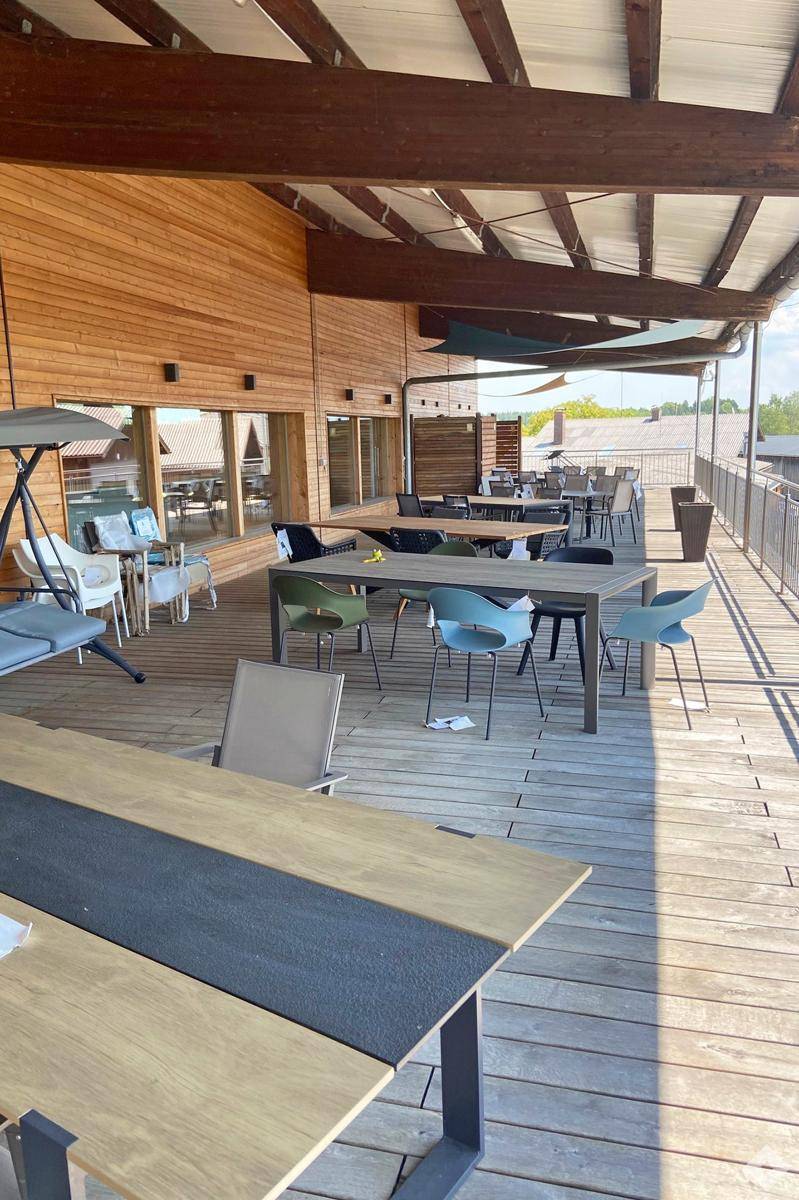 Große Holzterrasse mit zahlreichen Tischen und Stühlen, ideal für Außenbewirtung oder Entspannung.