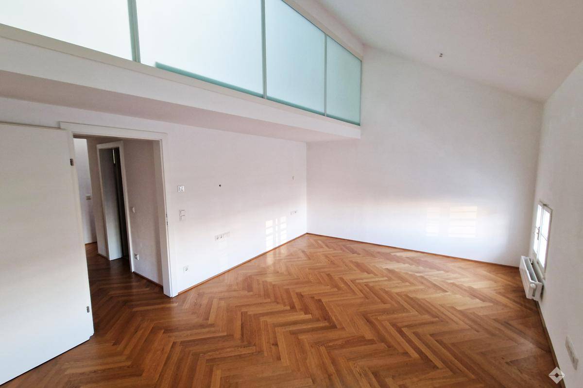 Großzügiger, heller Wohnbereich mit Fischgrätparkett und hoher Decke, offen zur oberen Galerie.