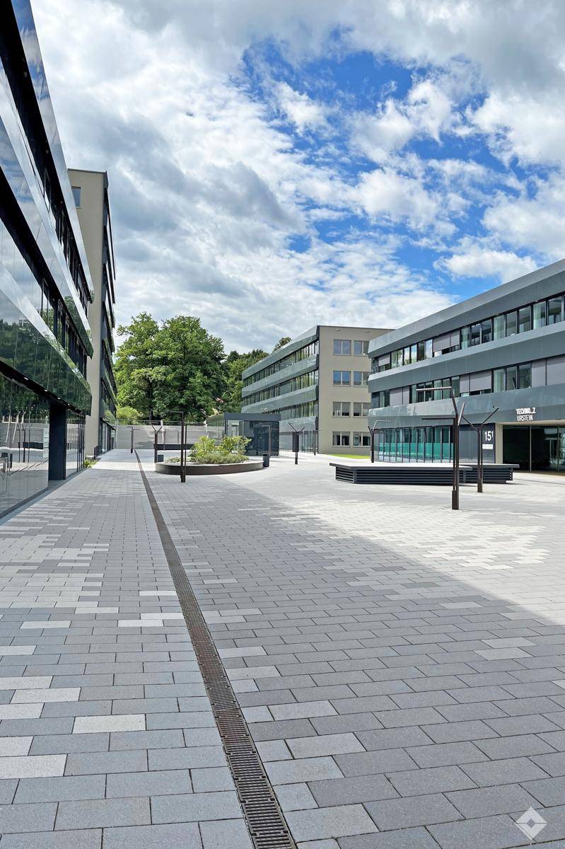 Moderner Bürokomplex mit gepflasterten Wegen, Grünflächen und zeitgenössischer Architektur unter blauem Himmel.