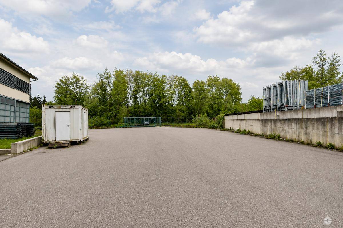 Großer asphaltierter Außenbereich neben einem Gebäude mit einem Container und einer Betonmauer im Hintergrund.