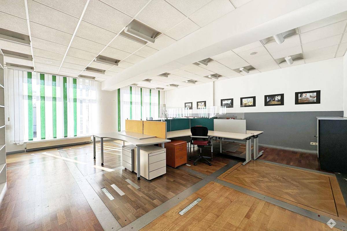 Heller Bürobereich mit Arbeitsplätzen, Holzparkett und grünen Jalousien, gut beleuchtet.