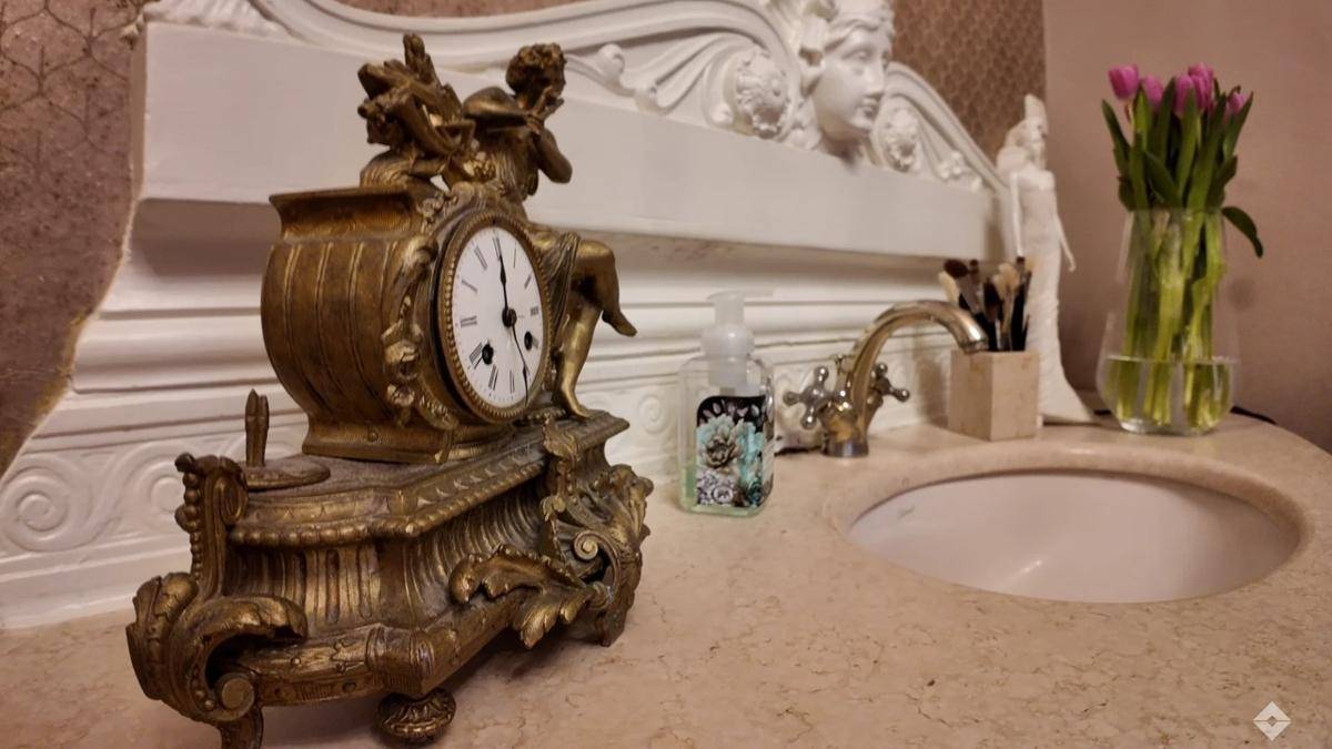Elegantes Badezimmer mit antikem Uhrwerk, Steinwaschtisch, klassischem Wasserhahn und dekorativem Spiegel, geschmückt mit frischen Tulpen.