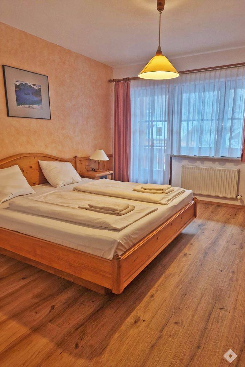 Helles Schlafzimmer mit Doppelbett, Holzfußboden und großem Fenster mit Vorhängen.